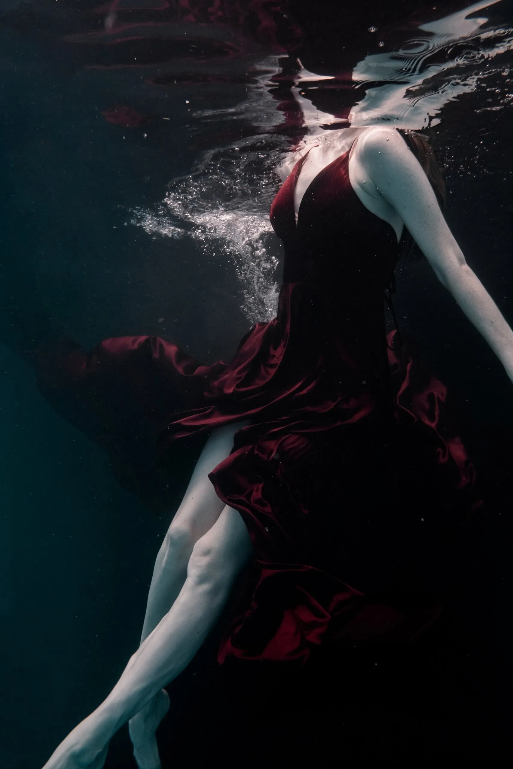A figure suspended underwater, fabric drifting in soft light